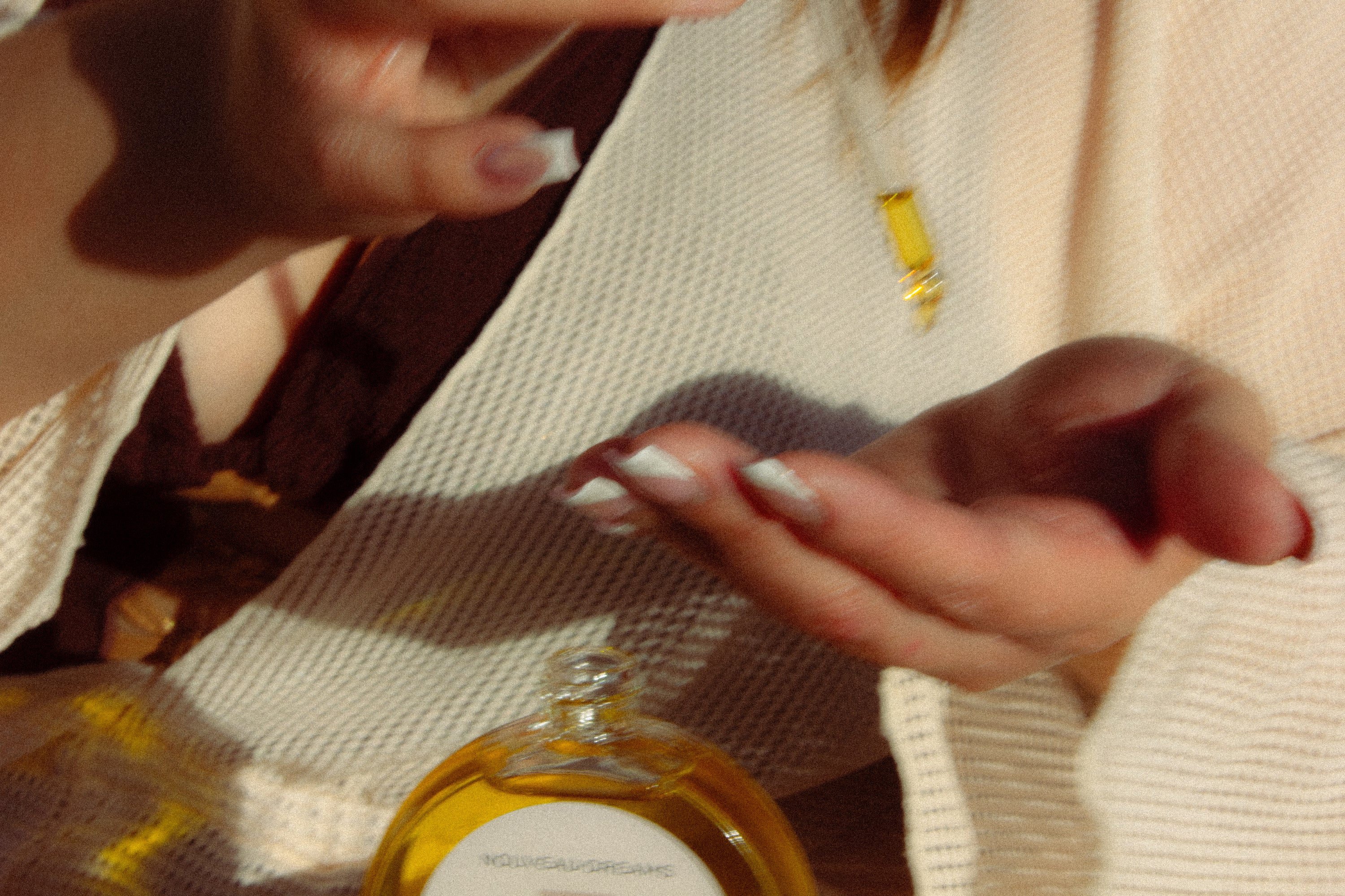 Close-up of hands applying Nouveau Dreams Argan Oil with a dropper in soft sunlight