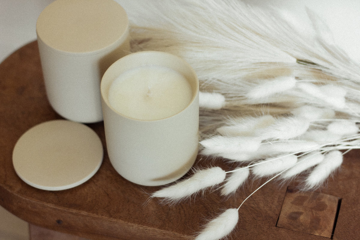Unlit cream-colored candles in matte jars styled with white dried florals on a wooden surface