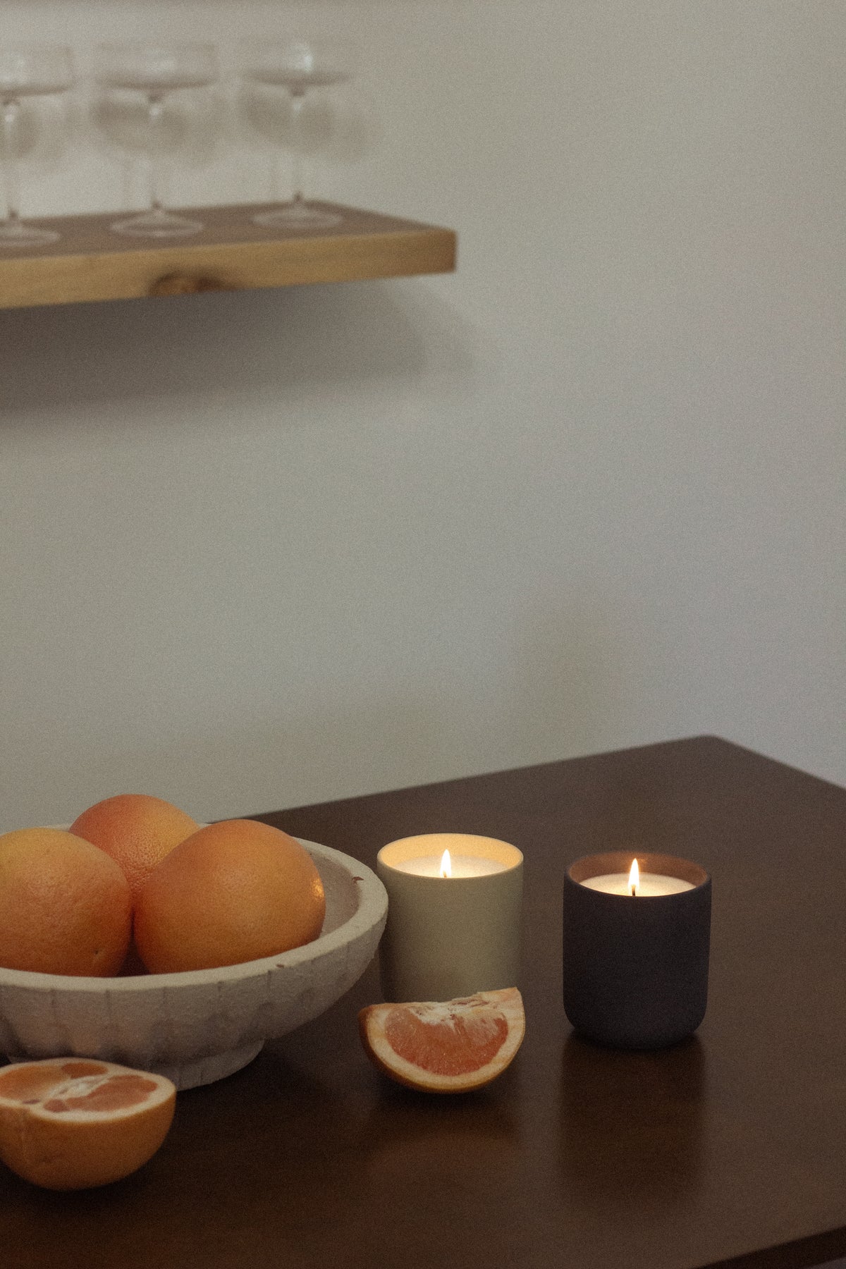 Two lit Nouveau Dreams candles beside a bowl of grapefruit and citrus slices on a wood table