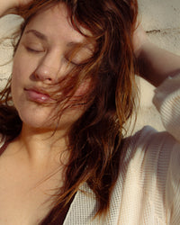 Close-up of woman with eyes closed, sun-kissed skin, and natural hair blowing gently in the breeze