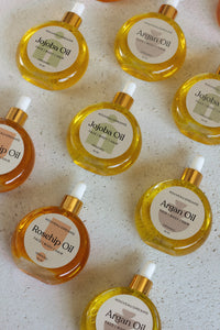 Flat lay of Nouveau Dreams organic oils in round glass bottles with dropper tops, including Argan, Jojoba, and Rosehip oil, 54ml each